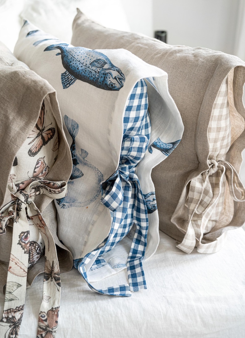 May include: Close-up of three decorative pillows with unique designs. One pillow features a blue fish print, another showcases a butterfly pattern, and the third has a neutral gingham pattern. Each pillow has a matching fabric tie.