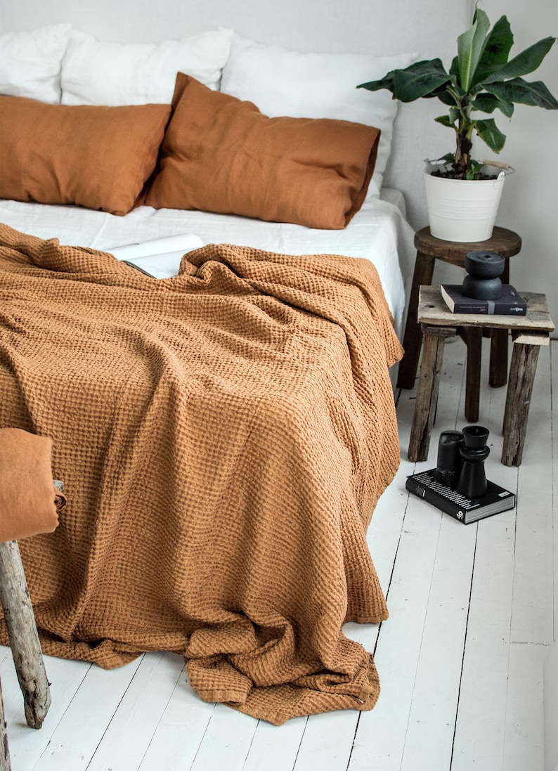 Pu&ograve; includere: Una coperta in tessuto a nido d'ape marrone drappeggiata su un letto bianco con cuscini marroni. La coperta &egrave; realizzata in un tessuto morbido e testurizzato e ha un aspetto naturale e terroso.
