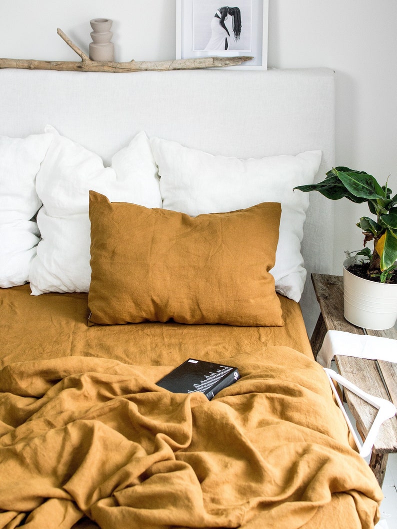 Puede incluir: Una funda n&oacute;rdica y fundas de almohada de lino amarillo mostaza en una cama con almohadas de lino blanco. Un libro est&aacute; colocado sobre la funda n&oacute;rdica.