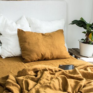 Puede incluir: Una funda n&oacute;rdica y fundas de almohada de lino amarillo mostaza sobre una cama blanca con una cabecera blanca. La cama est&aacute; hecha con una almohada de lino blanco y una almohada de lino amarillo mostaza.