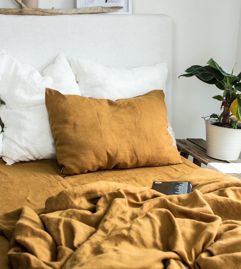 Puede incluir: Una funda n&oacute;rdica y fundas de almohada de lino amarillo mostaza sobre una cama blanca con una cabecera blanca. La cama est&aacute; hecha con una almohada de lino blanco y una almohada de lino amarillo mostaza.