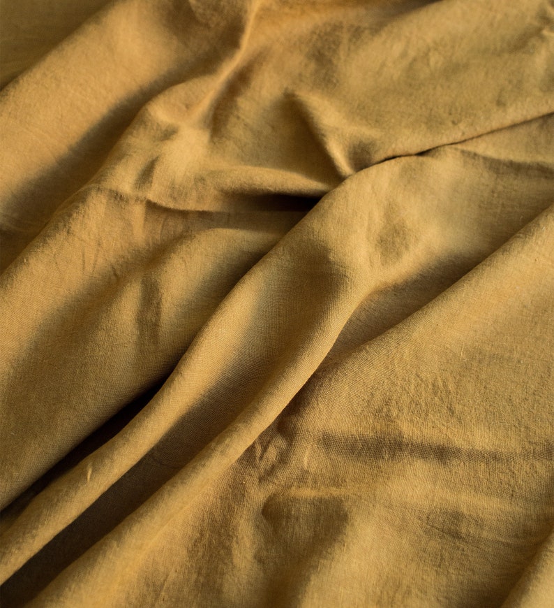 Puede incluir: Primer plano de un trozo de tela arrugado de color amarillo mostaza apagado. La tela tiene una textura suave, similar al lino.