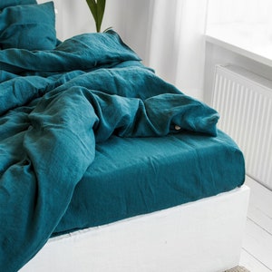 Könnte beinhalten: Ein Bettwäsche-Set aus tealfarbenem Leinen mit einem weißen Bettrock. Die Bettwäsche ist zerknittert und wirkt entspannt und lässig.