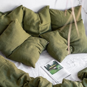 May include: A bed with a white linen duvet cover and several green linen pillows. The bed is styled with a magazine on top of the duvet.