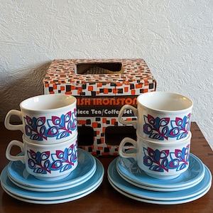 May include: A set of four white teacups with a blue and pink floral pattern. The cups are stacked on top of each other and are sitting on a blue and white saucer. The cups are part of a "Dish Ironstone Piece Tea/Coffee Set".