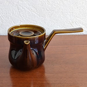 May include: A dark brown ceramic teapot with a lid and a spout. The teapot has a glossy finish and a rounded shape.