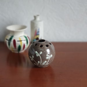 May include: A brown ceramic vase with a floral design and holes for flower stems. The vase is round and has a glossy finish.