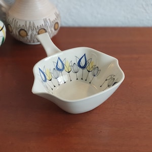 May include: A white ceramic serving dish with a blue and yellow tulip design. The dish has a handle and a square shape.