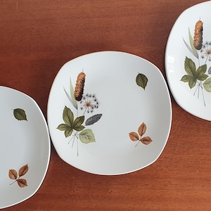 May include: Three white square plates with a floral design featuring brown, green, and white leaves and flowers.