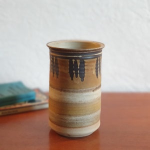 May include: A brown and white ceramic vase with a geometric pattern. The vase has a cylindrical shape and a slightly flared rim.