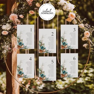 May include: Six white cards with floral designs and numbers 1 through 6 printed on them. The cards are hanging from a gold metal ring. The cards are likely for a wedding reception table seating chart.