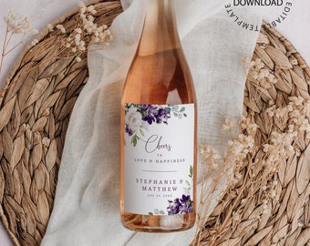 Può includere: Un'etichetta per bottiglia di vino stampabile con un design floreale in tonalità di viola e bianco. L'etichetta recita "Cheers to Love & Happiness" e include i nomi "Stephanie & Matthew" e la data "July 22, 20XX".