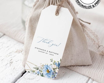 Può includere: Un'etichetta di ringraziamento bianca con calligrafia blu, accenti geometrici dorati e fiori blu ad acquerello. L'etichetta è attaccata a un piccolo sacchetto di juta. Il testo sull'etichetta recita "Grazie! Stephanie & Matthew 29 agosto 20XX".