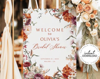 May include: A rectangular white bridal shower welcome sign featuring floral illustrations in shades of rust, burgundy, and cream. The text reads: WELCOME to OLIVIA'S Bridal Shower, SEPTEMBER 23, 20XX, MALIBU, CA. The sign hangs from a gold metal stand.