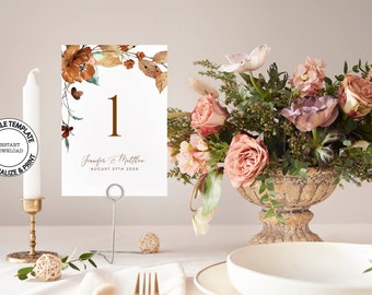 May include: A white wedding table number card with a brown floral design and the number "1" in gold. The card also includes the names "Jennifer & Matthew" and the date "August 27th 2020".