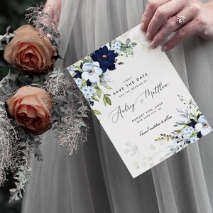 May include: A white save the date card with blue and white floral illustrations. The text reads "Kindly save the date for the wedding of Audrey & Matthew, August 17th, 2050, New York City, Formal invitation to follow."