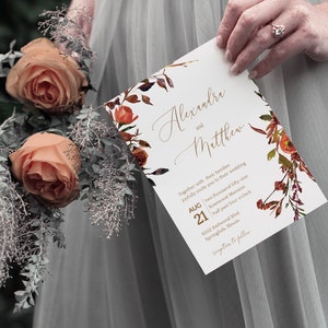 May include: A wedding invitation with a floral design in shades of orange, red, and brown. The invitation reads "Alexandra and Matthew" with the date "August 21" and the time "half past four o'clock".