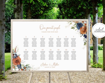 May include: A white wedding seating chart with a gold frame. The chart is decorated with a watercolor floral design in shades of blue, orange, and green. The text on the chart reads "Our favorite people, Please find your seat." and "Stephanie & Matthew, August 24, 20XX".
