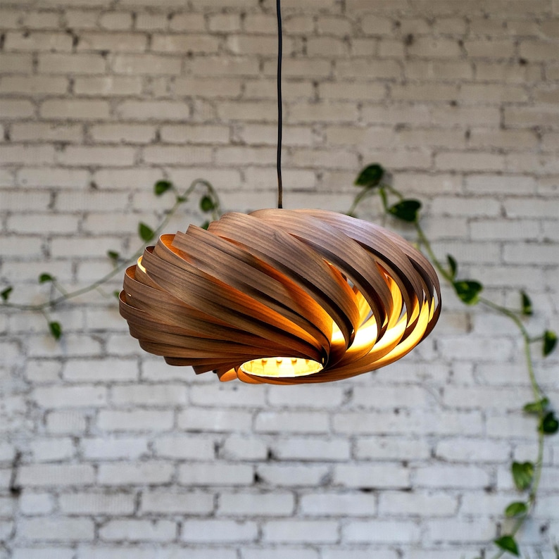 K&ouml;nnte beinhalten: Eine Holz-Pendelleuchte mit einem einzigartigen Spiraldesign. Die Leuchte besteht aus d&uuml;nnen Holzstreifen, die in einem wirbelnden Muster angeordnet sind. Die Leuchte ist eingeschaltet und strahlt ein warmes Licht aus.