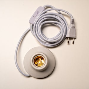 May include: White electrical cord with a white inline switch and a white plug. The cord is coiled and connected to a white ceramic light socket.