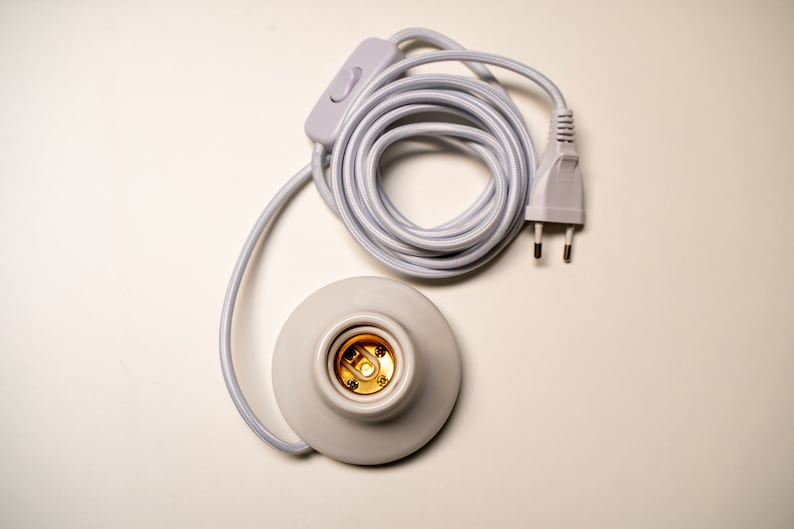 May include: White electrical cord with a white inline switch and a white plug. The cord is coiled and connected to a white ceramic light socket.