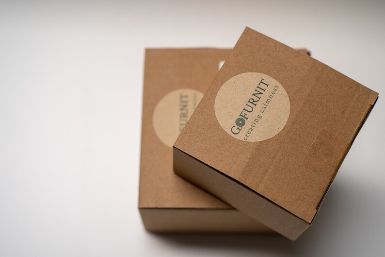May include: Two brown cardboard boxes stacked on top of each other. The top box has a round sticker with the text "GO FURNIT creating calmness".