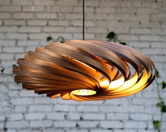 May include: A contemporary wooden pendant light. The light fitting is suspended from a black cable and has a spiral design made of layered wooden strips. The warm light shines through the gaps, creating a cosy atmosphere.