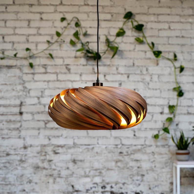 K&ouml;nnte beinhalten: Eine Holz-Pendelleuchte mit einem einzigartigen, wirbelnden Design. Die Leuchte besteht aus d&uuml;nnen Holzstreifen, die &uuml;bereinander gelegt und gebogen sind, um einen dreidimensionalen Effekt zu erzeugen. Die Leuchte wird von innen beleuchtet und erzeugt ein warmes Licht.