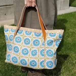 May include: A large tote bag with brown leather handles. The bag is made of a light blue and green fabric with a floral pattern.
