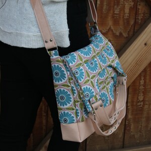 Puede incluir: Un bolso bandolera de estampado floral rosa y azul con una correa de cuero y detalles plateados.