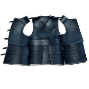 May include: Black leather armor vest with multiple layers of segmented plates. The vest is open in the back, showing the interior lining.