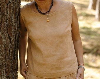 May include: A tan linen sleeveless top and matching shorts. The outfit is a neutral color and appears to be made of a lightweight fabric. The shorts have an elastic waistband. The person is wearing a necklace.