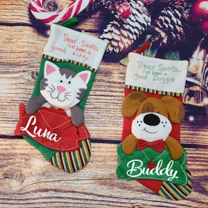 May include: Two Christmas stockings with pet-themed designs. One features a gray and white cat with the name "Luna", and the other a brown dog named "Buddy". Both stockings have the text "Dear Santa I've been a good" followed by "kitty" or "doggie".