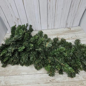 May include: A pile of artificial pine branches, perfect for crafting wreaths or garlands. The branches are a deep green color and have a realistic texture.