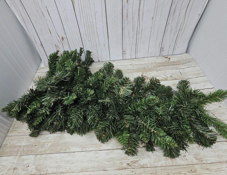 May include: A pile of artificial pine branches, perfect for crafting wreaths or garlands. The branches are a deep green color and have a realistic texture.