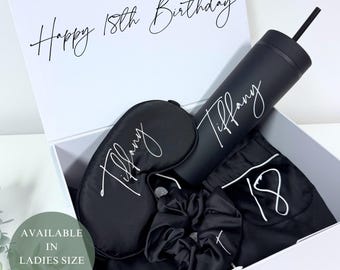 Puede incluir: Una caja de regalo negra que contiene un vaso negro con pajita, una máscara para dormir, una goma para el pelo y un pantalón de pijama. El vaso y la máscara para dormir están personalizados con el nombre "Tiffany". La tapa de la caja dice "Happy 18th Birthday".