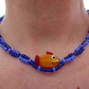 Puede incluir: Un collar de cuentas azules y moradas con un dije de pez naranja de vidrio.