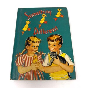 May include: A vintage hardback book titled Something Different with a teal cover. The illustration features a child in a red and white striped dress holding a yellow duckling and a child in a yellow shirt holding a grey kitten, with three yellow ducklings above.