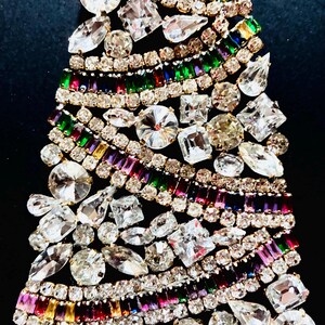 May include: A decorative brooch shaped like a Christmas tree, constructed from numerous clear, round, pear, and emerald-cut rhinestones alongside rows of multi-coloured baguette-cut crystals in shades of red, green, blue, purple, and yellow.