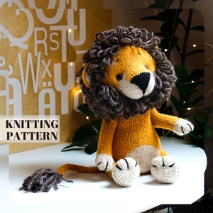 May include: A knitted lion toy with a brown mane, yellow body, and white paws. The toy is sitting on a white surface with a brown background.