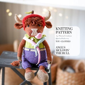 May include: A knitted bull toy, dressed in a red hat, green shirt, and purple trousers. The toy has horns, a tail, and a scarf. The image includes text stating "Knitting Pattern" and "Angus McLovin' The Bull".