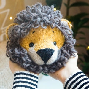 May include: A knitted lion head with a brown mane and a yellow face. The lion has black eyes and a black nose.