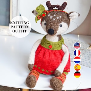 Könnte beinhalten: Strickanleitung für eine Hirschpuppe, die ein rotes Kleid mit grünen Akzenten und einer grünen Schleife trägt. Das Muster ist in Englisch, Französisch, Deutsch, Niederländisch, Spanisch und Italienisch verfügbar.