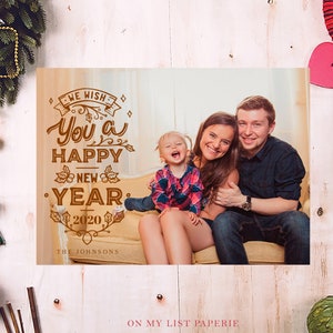 K&ouml;nnte beinhalten: Eine Weihnachtskarte mit einem Familienportr&auml;t und dem Text &bdquo;Wir w&uuml;nschen Ihnen ein frohes neues Jahr 2020&ldquo;. Die Familie l&auml;chelt. Festliche Dekorationen umgeben die Karte, darunter ein Kranz und Ornamente.