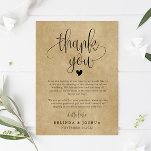May include: A thank you card with a rustic brown background and black text. The card says "Thank you" with a small black heart. The text reads "From the bottom of our hearts, we would like to thank you for sharing in the celebration of our wedding. We felt the love and sincerity all around us which made it the most memorable day of our lives. We are grateful for your presence, warm wishes and your generous gift and look forward to sharing many more memories with you. With love, Belinda & Joshua, November 14, 2022. On My List Paperie."