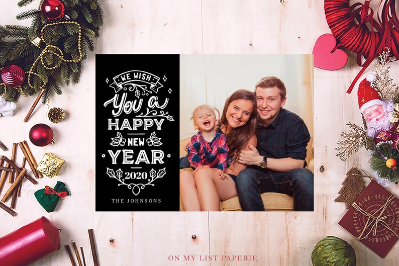 K&ouml;nnte beinhalten: Eine schwarz-wei&szlig;e Neujahrskarte mit dem Text "We wish you a Happy New Year 2020" und einem Familienportr&auml;t. Die Karte ist von Weihnachtsdekorationen umgeben, darunter ein Kranz, Ornamente und Zimtstangen.