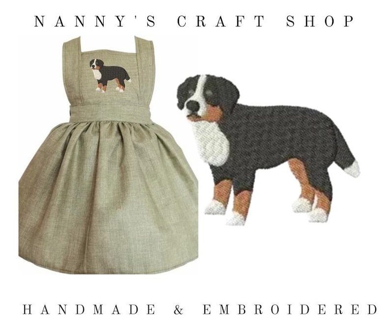 Op de afbeelding: Een saliegroene pinafore-jurk met een geborduurde Berner Sennenhond op de borst. De tekst NANNY'S CRAFT SHOP staat bovenaan en HANDMADE & EMBROIDERED onderaan. Een grotere versie van het hondenborduurwerk wordt apart weergegeven.