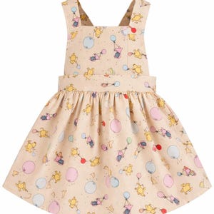 Pode incluir: Vestido bege claro com padr&atilde;o de Winnie the Pooh. O vestido apresenta um decote quadrado, al&ccedil;as cruzadas nas costas e uma saia franzida. O padr&atilde;o inclui Pooh, Piglet e bal&otilde;es em v&aacute;rias cores.