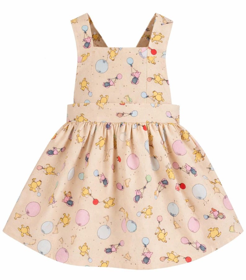 Pode incluir: Vestido bege claro com padr&atilde;o de Winnie the Pooh. O vestido apresenta um decote quadrado, al&ccedil;as cruzadas nas costas e uma saia franzida. O padr&atilde;o inclui Pooh, Piglet e bal&otilde;es em v&aacute;rias cores.