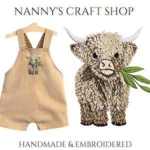 Pode incluir: Macac&atilde;o bege para beb&eacute; com um design bordado de vaca Highland, pendurado num cabide de madeira. Uma vaca Highland bordada detalhada com folhas verdes tamb&eacute;m &eacute; mostrada. O texto diz "Nanny's Craft Shop" e "Handmade & Embroidered".
